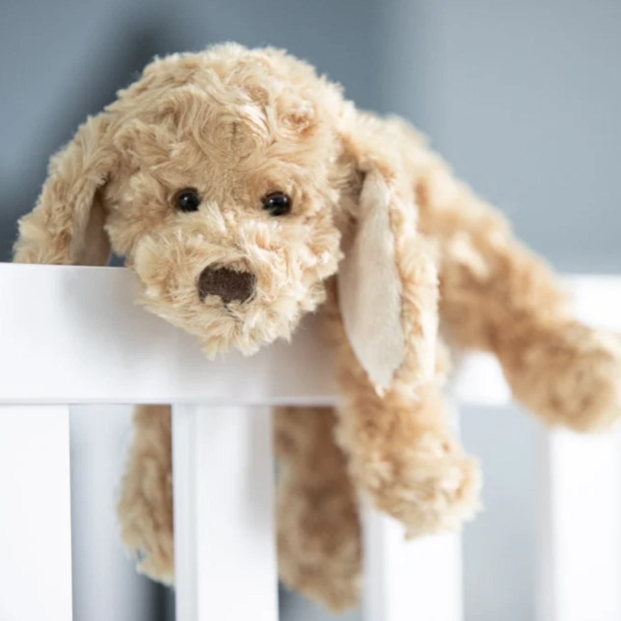 Buddy knuffelpuppy 25 cm van Bukowski Sweden met zachte krulvacht en flaporen hangend over een ledikant