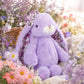 Friendly Karina Floral knuffelkonijn van Bukowskiknuffels.nl met lavendelkleurige pluche, bloemenprint in de hangoren, als strik en onder de pootjes, zittend in bloemenveld